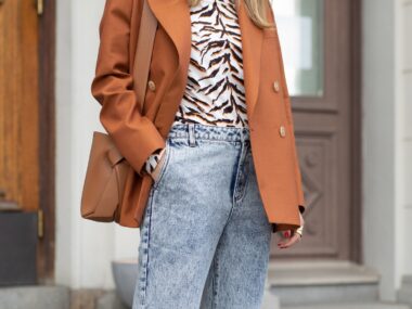 Acid wash jeans with a tan jacket and animal print blouse.