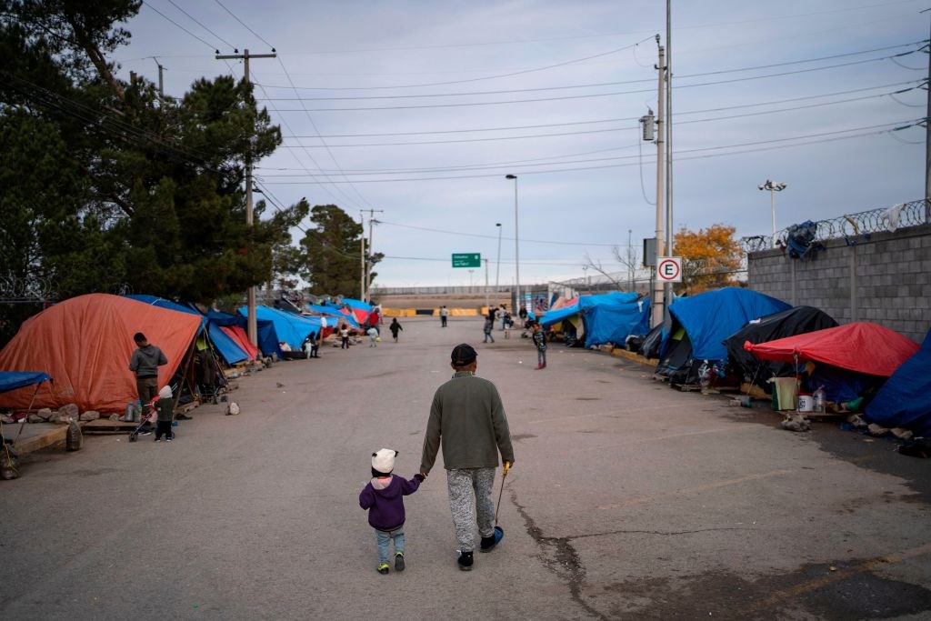 A man walks with his daugher at an asylum seekers camp near the Zaragoza bridge in Ciudad Juarez, Mexico