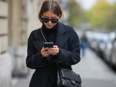 woman wearing black walks down street texting