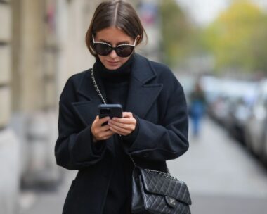 woman wearing black walks down street texting