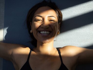 Woman smiling as she lies on her back in shadows.