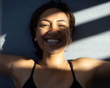 Woman smiling as she lies on her back in shadows.