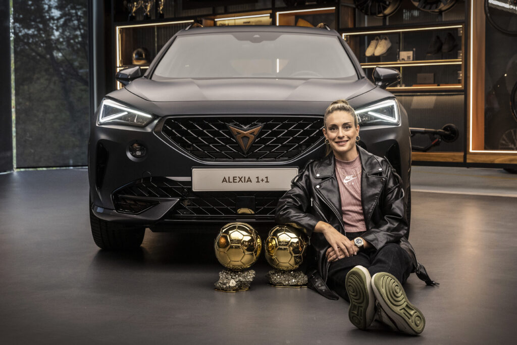 Alexia Putellas with her FIFA trophies sitting in front of a CUPRA car.
