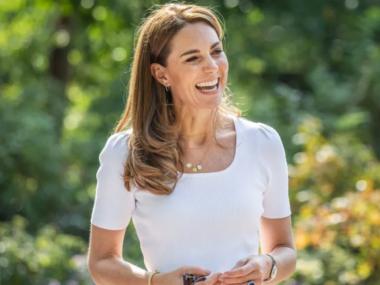 Kate middleton smiles while wearing a white, square-neck top