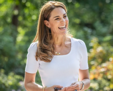 Kate middleton smiles while wearing a white, square-neck top