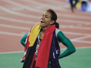 Cathy Freeman drapes the aboriginal and australian flags around her shoulders, smiling, at the 2000 sydney olympic games