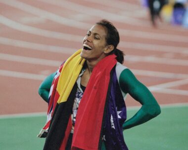 Cathy Freeman drapes the aboriginal and australian flags around her shoulders, smiling, at the 2000 sydney olympic games