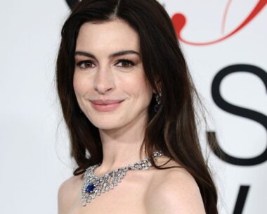 A close up of anne hathaway at the 2023 cfda awards. She looks toward the camera,smiling slightly with her brown hair loose around her shoulders and a large diamond necklace on
