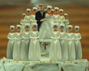 A teaser image from cult documentary 'keep sweet pray and obey' featuring a classic husband and wife wedding cake topper atop a cake, surreounded by more models of the wife doll.