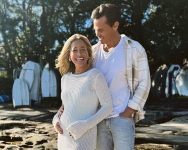holly kingston craddles a baby bump wearing a white crochet dress and standing next to husband Jimmy nicholson, who wears a white shirt, cream overshirt and light blue jeans