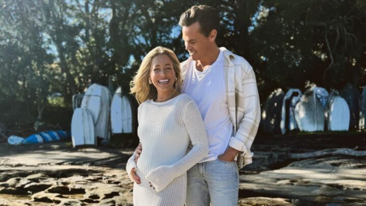 holly kingston craddles a baby bump wearing a white crochet dress and standing next to husband Jimmy nicholson, who wears a white shirt, cream overshirt and light blue jeans