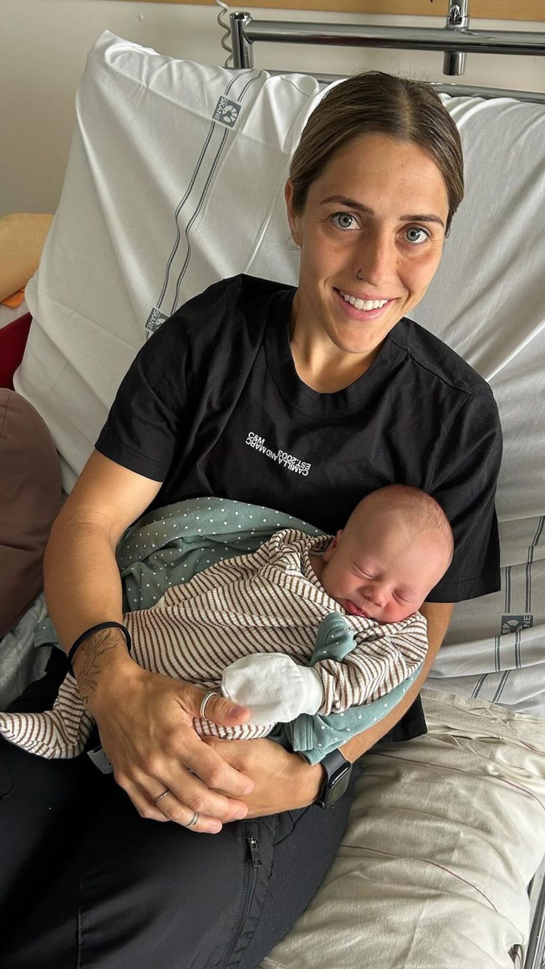 Matildas star katrina gorry sits in a hospital bed, smiling, while holding her baby boy