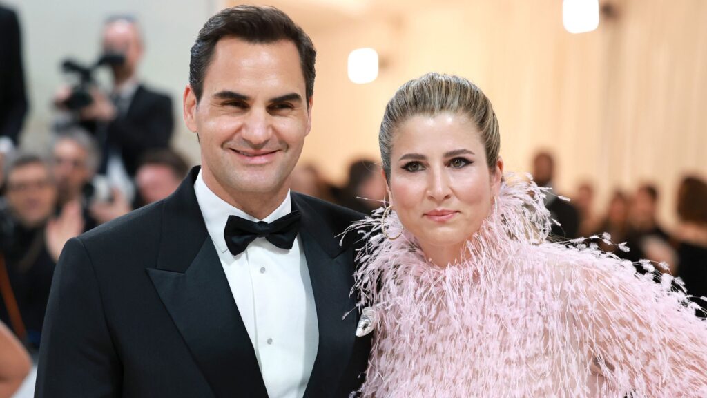 A close up shot of Roger Federer and his wife, Mirka at the 2023 met gala. He wears a black suit, white shirt and black bow tie. She wears a pink feathered gown