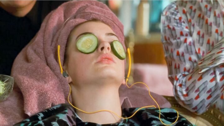 Anne Hathaway in The Princess Diaries having a self care moment with cucumber slices over her eyes, a towel wrapped around her and headphones in.