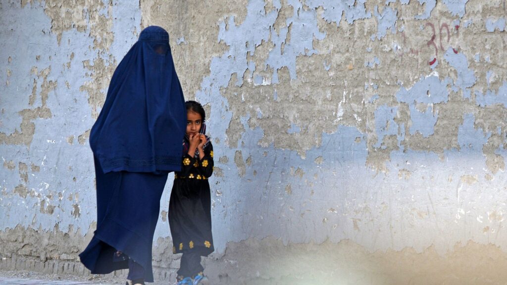 A burqa-clad woman walks with a girl along a street in Kabul on May 7, 2022. - The Taliban on May 7 imposed some of the harshest restrictions on Afghanistan's women since they seized power, ordering them to cover fully in public, ideally with the traditional burqa.