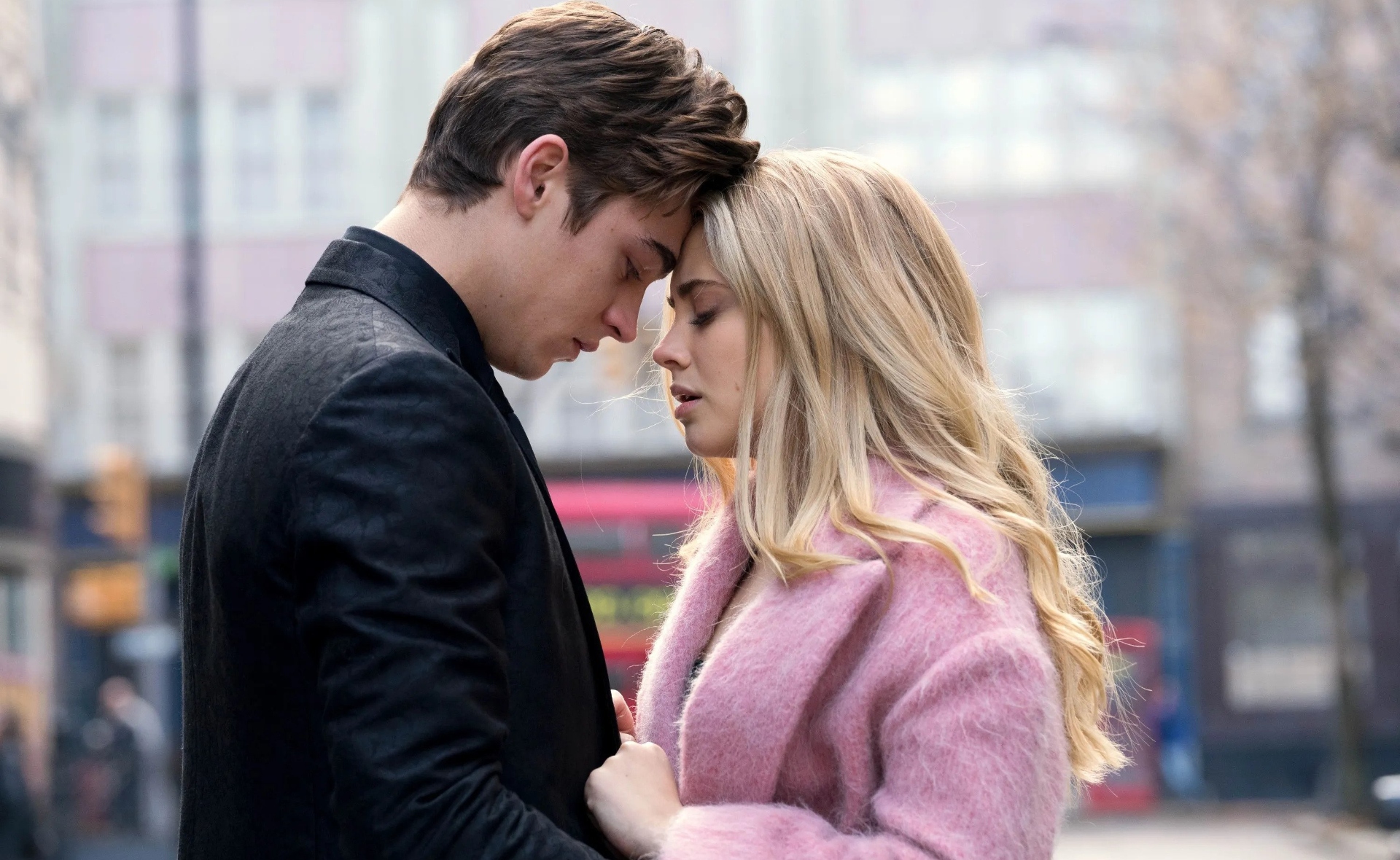 A young couple in an emotional embrace with their foreheads touching, standing on a city street.