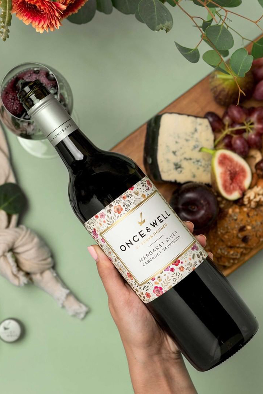 hand holding bottle of once and well cabernet wine with cheese and figs in background