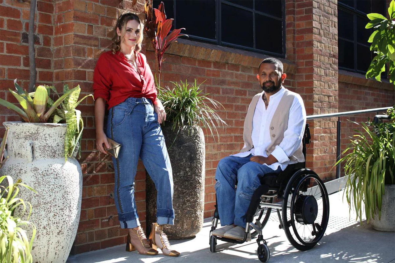 woman in red shirt standing next to man in wheel chair